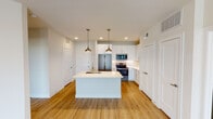 Located in Trophy Club, TX, this well-designed single-floor residence offers a clean, contemporary aesthetic throughout. The open-concept kitchen serves as the heart of the home, showcasing crisp white cabinetry, a decorative mosaic tile backsplash, stainless steel appliances including a French door refrigerator and range, and a central island with a built-in sink and pendant lighting overhead. A dedicated wine rack and ample cabinet storage add functional character to the space. Warm hardwood-style flooring flows through the kitchen and living areas, creating a cohesive and inviting atmosphere. The living area is generously sized and connects seamlessly to adjacent spaces, with recessed lighting providing a bright, airy feel. Bedrooms feature plush carpeting, ceiling fans, and windows that bring in natural light and outdoor views of the surrounding landscape. The primary bathroom is well-appointed with a dual-area layout, a soaking tub, a glass-enclosed shower with tile surround, a white vanity with quartz countertops, and direct access to a walk-in closet. A second full bathroom mirrors the refined finishes with a tiled tub/shower combo, white cabinetry, and a large framed mirror. Throughout the residence, neutral tones, modern hardware, and thoughtful details create a polished and comfortable living environment.