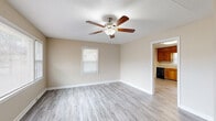 Located at 318 Richlands Ave in Jacksonville, NC, this single-floor, 2-bedroom, 1-bathroom home offers a practical and comfortable layout designed for easy everyday living. The living room serves as a welcoming centerpiece, featuring light gray luxury vinyl plank flooring, a ceiling fan with built-in lighting, and large windows that allow generous natural light to fill the space. A front entry door with a decorative glass insert adds a charming touch to the entryway. The kitchen is well-appointed with warm honey-toned wood cabinetry extending to the ceiling for ample storage, black appliances including a range, dishwasher, and built-in open shelving, all complemented by light-toned LVP flooring. Both bedrooms are carpeted for comfort and include ceiling fans. The primary bedroom features dual sliding closets, offering notable storage capacity, while the second bedroom benefits from multiple windows that bring in plenty of natural light. The bathroom includes a full tub and shower combination with white tile surround. A standout feature is the dedicated laundry room, complete with shiplap-style wall paneling, windows on two sides, and space for a full-size washer and dryer. The home's neutral warm-beige palette throughout creates a cohesive and inviting atmosphere.