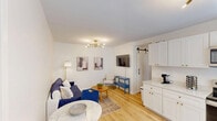 Located at 3005 Leonard Street in Raleigh, NC, this single-floor home offers a well-organized layout with 2 bedrooms, 2 bathrooms, a kitchen, living room, hallway, and closet. Light hardwood flooring runs throughout, creating a cohesive and airy aesthetic across every room. The kitchen is a standout feature, outfitted with crisp white shaker cabinets with gold hardware, stainless steel appliances including a range, microwave, dishwasher, and refrigerator, plus open shelving and a sliding barn door accent. A sputnik-style chandelier adds a modern touch overhead. The living room is bright and welcoming, featuring the same contemporary chandelier, clean white walls, and curated wall art. Both bedrooms are comfortably sized, filled with natural light from large windows with outdoor greenery views, and equipped with wall-mounted mini-split units for individual climate control. The primary bedroom offers a cozy yet functional space. The bathrooms are cleanly finished, with one featuring elegant marble-style tile surrounding a full soaking tub and shower with brushed nickel fixtures. The overall ambiance is clean, modern, and inviting, making this a well-appointed home in a convenient Raleigh location.