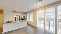 Located at 603 Rigsbee Ave in Durham, NC, this single-floor unit showcases a contemporary design with a cohesive, open-concept layout. Polished concrete floors run throughout the main living areas, lending an industrial-modern aesthetic that contrasts cleanly with the warm, neutral-toned walls.

The kitchen is well-appointed with stainless steel appliances, including a range, microwave, and refrigerator. White cabinetry with sleek hardware pairs with granite countertops that extend across a peninsula island, which doubles as a breakfast bar. Pendant lighting hangs above the island, while track lighting illuminates the surrounding space. A tile backsplash adds a refined finishing detail near the cooking area.

The open living area is bright and airy, benefiting from multiple large windows fitted with blinds and direct access to a private balcony through sliding glass doors. The views look out toward the surrounding Durham streetscape. Track and ceiling-mounted lighting provide flexible illumination throughout.

The bedroom features plush carpeting, a ceiling fan with integrated light, and a generously sized window that draws in natural light. The bathroom includes a granite-topped vanity with an undermount sink, a tub-shower combination with large-format tile surround, and consistent concrete flooring.