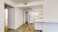 Located at 15082 N 59th Ave in Glendale, Arizona, this efficient one-bedroom, one-bathroom unit offers a well-organized single-floor layout. Wood-look plank flooring runs throughout the living areas and bedroom, providing a cohesive and clean aesthetic. The living room features a ceiling fan with light fixture, a textured ceiling, and a large vertical-blind-covered window that allows natural light to fill the space. A front entry door opens directly into this welcoming area. The kitchen is thoughtfully designed with white upper and lower cabinetry, a refrigerator, dishwasher, single-basin sink, and a white countertop peninsula that separates the kitchen from the living area. An adjacent open shelving unit offers additional storage. A dedicated closet features built-in shelving and corner storage, maximizing organizational potential. The bedroom is a comfortable, well-proportioned room with wood-look flooring, a window with vertical blinds, and a textured ceiling. The bathroom includes a full-size tub and shower combination with clean white surround walls and chrome fixtures. Throughout the unit, neutral wall tones and white trim create a bright, functional living environment.