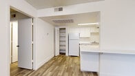 Located at 15082 N 59th Ave in Glendale, Arizona, this efficient one-bedroom, one-bathroom unit offers a well-organized single-floor layout. Wood-look plank flooring runs throughout the living areas and bedroom, providing a cohesive and clean aesthetic. The living room features a ceiling fan with light fixture, a textured ceiling, and a large vertical-blind-covered window that allows natural light to fill the space. A front entry door opens directly into this welcoming area. The kitchen is thoughtfully designed with white upper and lower cabinetry, a refrigerator, dishwasher, single-basin sink, and a white countertop peninsula that separates the kitchen from the living area. An adjacent open shelving unit offers additional storage. A dedicated closet features built-in shelving and corner storage, maximizing organizational potential. The bedroom is a comfortable, well-proportioned room with wood-look flooring, a window with vertical blinds, and a textured ceiling. The bathroom includes a full-size tub and shower combination with clean white surround walls and chrome fixtures. Throughout the unit, neutral wall tones and white trim create a bright, functional living environment.