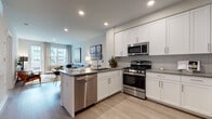 Located at 1000 Schindler Dr in South Amboy, New Jersey, this thoughtfully designed single-floor residence offers a contemporary open-concept layout that seamlessly connects the kitchen, dining, and living areas. The kitchen is a standout feature, boasting crisp white shaker cabinetry, sleek gray countertops, a herringbone tile backsplash, and a full suite of stainless steel appliances including a gas range, built-in microwave, dishwasher, and a large refrigerator. A peninsula with an integrated sink provides additional prep space and doubles as a casual dining counter. Light wood-toned flooring flows throughout, complementing the neutral palette and recessed lighting overhead. The open living and dining area is bright and welcoming, with large windows that invite natural light and offer views of the surrounding community. The living space accommodates generous seating and connects to a balcony access point. The bedroom features a wide window with soft draping, providing ample natural light and a restful atmosphere. A second bedroom offers comfortable proportions and additional natural light. The bathroom is finished with neutral tile flooring, built-in shelving, and clean, modern fixtures, creating a calm and functional space. Overall, the residence presents a polished, contemporary aesthetic throughout.
