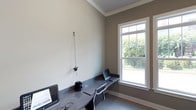 This business center is a thoughtfully designed, single-floor workspace that combines functionality with a clean, professional aesthetic. The room features neutral taupe and cream-toned walls accented by crisp white crown molding and baseboards, lending the space a polished, refined character.

At the heart of the room is a built-in granite countertop workstation that spans the length of the wall, offering generous workspace for multiple users. The dark, speckled granite surface provides a durable and stylish work surface, complemented by ergonomic task chairs that ensure comfort during extended use. Workstations are equipped with computer setups, making the space ready for immediate professional use.

A large, white-trimmed double-hung window serves as a standout feature, flooding the room with abundant natural light and offering a pleasant view of the surrounding outdoor greenery. The window's transom-style upper panes add an architectural detail that enhances the room's overall design. The light tile flooring further brightens the space and contributes to its clean, orderly atmosphere.

Overall, this business center delivers a quiet, well-lit, and efficiently arranged environment suited for focused work, making it a valuable and practical amenity.