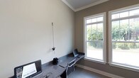 This business center is a thoughtfully designed, single-floor workspace that combines functionality with a clean, professional aesthetic. The room features neutral taupe and cream-toned walls accented by crisp white crown molding and baseboards, lending the space a polished, refined character.

At the heart of the room is a built-in granite countertop workstation that spans the length of the wall, offering generous workspace for multiple users. The dark, speckled granite surface provides a durable and stylish work surface, complemented by ergonomic task chairs that ensure comfort during extended use. Workstations are equipped with computer setups, making the space ready for immediate professional use.

A large, white-trimmed double-hung window serves as a standout feature, flooding the room with abundant natural light and offering a pleasant view of the surrounding outdoor greenery. The window's transom-style upper panes add an architectural detail that enhances the room's overall design. The light tile flooring further brightens the space and contributes to its clean, orderly atmosphere.

Overall, this business center delivers a quiet, well-lit, and efficiently arranged environment suited for focused work, making it a valuable and practical amenity.