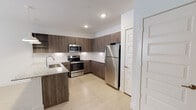 This single-floor residence showcases a contemporary design with a cohesive color palette of whites, light wood tones, and warm cabinetry finishes. The kitchen serves as a centerpiece of the space, outfitted with full-height wood-grain cabinetry providing generous storage, a granite-topped peninsula island with an undermount sink, and a full suite of stainless steel appliances including a refrigerator, range, and built-in microwave. Recessed lighting and elegant pendant lights above the island illuminate the space, complemented by a clean white tile backsplash. Light wood-look flooring runs throughout the main living areas, contributing to a bright and airy atmosphere.

The entryway is clean and functional, with light flooring and direct access to adjacent rooms. A dishwasher is conveniently integrated near the kitchen entry. The bedroom features plush neutral carpeting, a ceiling fan with integrated light, and a sliding-door closet with built-in shelving, offering practical storage. The bathroom is finished with light wood-look flooring, a full-sized soaking tub and shower combination with white tile surround, and brushed nickel fixtures. Overall, the space presents a clean, modern aesthetic well-suited for comfortable everyday living.