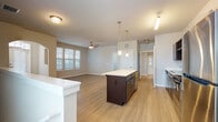 This single-floor residence offers a thoughtfully designed open-concept layout that seamlessly connects the kitchen and living areas. The kitchen serves as the centerpiece of the home, showcasing dark espresso cabinetry, a built-in wine rack, stainless steel appliances including a refrigerator, range, and microwave, and a generous island topped with a light marble-style surface. Pendant lighting above the island and a track light fixture add a polished, modern touch. Light wood-look flooring extends throughout the main living areas, complementing the neutral warm-toned walls.

The living area is bright and open, benefiting from multiple windows fitted with horizontal blinds that allow natural light to filter in. A ceiling fan adds comfort to the space. An elegant arched doorway connects the main living zone to an additional room, adding architectural character to the layout.

The bedrooms are carpeted for comfort and feature ceiling fans, large windows with ample natural light, and a calm, neutral color palette. The bathroom is well-appointed with dark vanity cabinetry, a light countertop, a framed mirror, and contemporary fixtures, all set against light wood-look flooring. Overall, the space presents a clean, modern aesthetic with consistent finishes throughout.