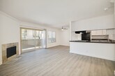 This single-floor, one-bedroom unit offers a thoughtfully designed layout that maximizes its compact footprint. The open-concept living and kitchen area forms the heart of the home, where light gray laminate flooring flows seamlessly throughout, lending a clean, modern aesthetic. The living room is highlighted by a tile-surround fireplace and crown molding, while sliding glass doors lead to a private balcony, filling the space with natural light and providing outdoor views.

The kitchen is efficiently arranged in a galley-style configuration, featuring white cabinetry, dark granite-style countertops, black stainless appliances including a refrigerator and range, and a bold overhead range hood. A peninsula counter extends into the living area, creating a natural boundary between the two spaces and offering additional prep or serving surface.

The bedroom is a comfortably sized, bright retreat with a window overlooking greenery and easy access to a generously sized walk-in closet. The closet is outfitted with built-in shelving and hanging rods, providing ample storage. Neutral wall tones and consistent flooring throughout the unit create a cohesive, move-in-ready atmosphere that is both functional and inviting.