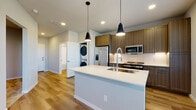 Located on Foxtail Palm Way in Bradenton, Florida, this single-story residence showcases a thoughtfully designed open-concept layout with contemporary finishes throughout. Light wood-tone flooring flows seamlessly through the main living areas, complemented by neutral gray walls and crisp white trim that create a clean, modern aesthetic.

The kitchen serves as a central hub of the space, featuring a large island with a white quartz countertop, an undermount sink, and a sleek pull-down faucet. Warm wood-toned cabinetry extends floor to ceiling, providing ample storage, while white subway tile backsplash adds a classic contrast. Stainless steel appliances include a side-by-side refrigerator with ice maker, a range, and a built-in microwave. A stacked washer and dryer unit is conveniently situated just off the kitchen. Pendant lighting above the island adds a refined touch. The open living area receives natural light through multiple windows fitted with blinds and includes a ceiling fan for comfort.

Bedroom spaces offer plush carpeting and organized closets with built-in shelving. The bathroom is finished with a wood-toned vanity, white quartz countertop, a backlit mirror, and a tiled tub-shower combination, maintaining the residence's cohesive modern design throughout.