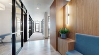 Located at 2358 Bransford Ave in Nashville, TN, this thoughtfully designed single-floor amenity space offers a polished, contemporary environment suited for both community gathering and everyday functional needs. The layout flows seamlessly from a welcoming corridor entrance — lined with black-framed glass partitions, warm wood-paneled accent walls, and modern sconce lighting — into a series of distinct yet interconnected areas.

A generous lounge area anchors the space, featuring plush neutral seating, patterned area rugs over light wood-look flooring, and pendant lighting that creates an inviting atmosphere. Adjacent glass-enclosed conference rooms with floor-to-ceiling windows allow abundant natural light and outdoor views, while maintaining a professional setting equipped with large conference tables and ergonomic seating.

A standout communal bar and café area showcases a striking teal mosaic tile backsplash, warm wood cabinetry, and a long counter with leather and upholstered bar seating beneath geometric pendant lights. Nearby, individual workstations with compact desks and blue accent chairs offer quiet focus areas complemented by framed black-and-white Nashville photography.

A dedicated mail center provides an extensive array of individual mailboxes, accented by cove lighting and live greenery. Throughout, the design balances warm wood tones, concrete textures, and crisp white finishes to create a sophisticated yet functional communal environment.