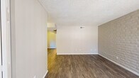 Located at 2345 N Craycroft Rd in Tucson, Arizona, this single-floor unit offers a practical and comfortable layout designed for everyday living. Consistent wood-look flooring flows throughout the living areas, providing a warm and cohesive aesthetic. The spacious living room is a standout space, featuring a distinctive painted brick accent wall that adds texture and character, along with a large sliding glass door fitted with vertical blinds that allows natural light to filter in and provides access to the outdoors. A large front window further brightens the entry area. The kitchen is efficiently designed in a U-shaped layout, outfitted with white cabinetry, dark countertops, a tile backsplash, and white appliances including a refrigerator, electric range, and dishwasher. A window above the sink brings in additional natural light. The bathroom is cleanly appointed with a full tub-and-shower combination, a white vanity with dark countertop, and a large mirror. Textured ceilings are present throughout, and ceiling vents indicate a central HVAC system. The overall layout, as seen in the dollhouse view, connects the living, dining, and kitchen areas in an open and functional arrangement, making efficient use of the available space.