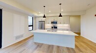 This well-appointed three-bedroom, two-bathroom residence is thoughtfully designed across a single floor, offering a clean, modern aesthetic throughout. The open-concept kitchen and living area serves as the heart of the home, featuring white shaker cabinetry, a large center island with a built-in sink and white countertops, stainless steel appliances including a French door refrigerator and built-in microwave, and a classic subway tile backsplash. Pendant lighting above the island and recessed ceiling lights add warmth to the space, while light-toned hardwood flooring runs throughout the main areas.

The primary bedroom is a comfortable retreat with large picture windows that invite natural light and offer views of the surrounding neighborhood. A sliding glass door in one of the bedrooms opens to a private balcony, extending the living space outdoors. The secondary bedrooms feature plush carpeting and windows for natural light. A central hallway connects all rooms efficiently, lined with clean white doors accented with matte black hardware.

The bathrooms are finished with wood-tone flooring, a glass-enclosed shower, and a wide vanity with ample cabinetry and a large mirror. A dedicated laundry room includes a full-size washer and dryer with overhead shelving, adding everyday convenience to this move-in-ready home.