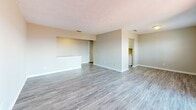 Located at 1191 Carlton Arms Circle in Bradenton, Florida, this single-floor residence offers a practical and well-organized layout with one bedroom, two bathrooms, and a dedicated living room. The living area is finished with light gray wood-look flooring and neutral-toned walls, creating a clean and cohesive aesthetic throughout the main space. A pass-through opening connects the living area to an adjacent space, adding an open, airy feel. A standout feature of the living room is the sliding glass door that floods the space with natural light and provides direct access to a private fenced patio, offering pleasant outdoor views. The spacious primary bedroom is carpeted for comfort and includes a window that brings in additional natural light, along with direct access to one of the two bathrooms. The en-suite bathroom features a tiled shower-tub combination, wood-look vinyl flooring, and a separate vanity area with a light-colored countertop, white cabinetry, and an oval mirror. The second bathroom mirrors a similar clean and functional design. Textured ceilings are present throughout the home, adding a subtle design element. An in-unit laundry area is also visible, adding everyday convenience to this well-appointed Bradenton residence.