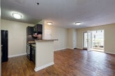 This single-floor residence offers a thoughtfully designed layout that balances open communal spaces with comfortable private quarters. The living and dining areas are unified by rich hardwood-style flooring that flows throughout the main spaces, creating a warm and cohesive aesthetic. A pendant light fixture anchors the dining area, while sliding glass doors invite natural light and provide access to an outdoor patio. The kitchen is designed in a galley configuration, featuring dark espresso cabinetry, granite-style countertops, a mosaic tile backsplash, and black appliances including a refrigerator and electric range. A peninsula counter connects the kitchen to the open living area, enhancing the sense of space and functionality. Two bedrooms offer a retreat from the main living spaces, each carpeted for comfort and equipped with windows that allow natural light to filter in. The primary bedroom connects directly to a dual-sink bathroom, complete with dark wood vanity cabinetry, granite-style countertops, and hardwood-style flooring. A second full bathroom features a combined tub and shower with grab bars, a single-sink vanity, and matching finishes. Textured ceilings and neutral warm-beige walls are consistent throughout, lending the residence a clean, move-in-ready appearance.