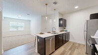 Located at 3111 Hayden Rd in Columbus, Ohio, this well-appointed 2-bedroom, 3-bathroom residence offers a thoughtfully designed single-floor layout. The open-concept living and kitchen area serves as the heart of the home, where light-toned luxury vinyl plank flooring flows seamlessly underfoot. The kitchen is a standout feature, boasting dark espresso cabinetry, crisp quartz countertops, stainless steel appliances including a refrigerator, range, microwave, and dishwasher, and a central island illuminated by two globe pendant lights with gold accents — ideal for both meal prep and casual dining. The adjoining living area transitions to plush carpeting and receives natural light through a window overlooking the exterior. Both bedrooms are carpeted and offer a clean, neutral palette with natural light from windows with blinds. The primary bedroom is generously sized and includes a walk-in closet fitted with wire shelving and hanging rods. The three bathrooms are finished with dark vanity cabinetry, quartz countertops, and LVP flooring, with tub/shower combinations. A dedicated laundry area and hallway add to the functional layout of this modern, move-in-ready home.