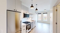Located on the fourth floor at 1050 W Wilson Ave in Chicago's Uptown neighborhood, this modern unit offers a thoughtfully designed single-level layout with clean, minimalist finishes throughout. Light hardwood flooring runs continuously across the living and sleeping areas, contributing to a bright and cohesive aesthetic. The open kitchen is a standout feature, equipped with a Blomberg refrigerator, stainless steel gas range and oven, integrated dishwasher, and a stainless steel sink. White cabinetry is complemented by subway tile backsplash and open metal bracket shelving, adding both function and contemporary style. Pendant lighting in a matte black dome finish illuminates the kitchen and living area, which receives generous natural light through large windows overlooking neighboring architecture and greenery. The bedroom features a wall-mounted ductless mini-split HVAC unit, a large window with views of the surrounding treetops, and a spacious closet with built-in shelving and hanging rods. An additional closet near the entry provides further storage. The bathroom is finished with polished concrete flooring, a sleek white vanity with under-cabinet storage, a large mirror, and a minimalist toilet. A frosted glass panel door adds privacy while maintaining an open feel.