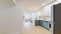 This single-floor residence showcases a thoughtfully designed open-concept layout that seamlessly connects the kitchen and living areas. The kitchen is a standout feature, boasting two-tone cabinetry with sage green lower cabinets and crisp white upper cabinets, all accented with gold hardware. A marble-look tile backsplash adds elegance, while stainless steel appliances — including a gas range, built-in microwave, dishwasher, and full-size refrigerator — provide modern functionality. White quartz countertops and a stainless steel sink complete the space.

Light hardwood flooring runs throughout the main living areas, enhancing the bright, airy atmosphere created by recessed lighting and large windows that invite abundant natural light. The living area offers a comfortable, open setting with views to the outdoors.

Two well-proportioned bedrooms feature large windows with roller shades, providing privacy while maintaining a connection to the outside. One bedroom includes access to a generous walk-in closet outfitted with wire shelving for ample storage.

The bathroom features warm wood-look tile flooring, white walls, and clean, contemporary fixtures. Throughout the residence, a consistent palette of whites and neutrals creates a cohesive, modern aesthetic that feels both fresh and inviting.