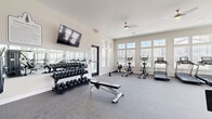 Located at 5353 N US Highway 27 in Ocala, Florida, this single-story fitness center offers a comprehensive and thoughtfully designed exercise facility across a generous floor area. The space is organized into three distinct zones, each serving a specific wellness purpose.

The main workout floor is the heart of the facility, featuring durable rubber flooring, ceiling fans, and an abundance of natural light streaming through large, multi-pane windows along the perimeter walls. This area is equipped with a full row of treadmills and elliptical trainers, a cable machine and weight bench station, a complete dumbbell rack, and wall-mounted flat-screen televisions. Mirrors line one wall to support strength training and form awareness.

A dedicated flex and yoga studio adjoins the main floor, finished with warm wood-look flooring and featuring a wall-mounted TV, fitness ball storage, and open floor space ideal for stretching, yoga, or group classes. The room maintains a calm ambiance enhanced by natural light and minimalist décor.

A children's area provides a comfortable, supervised space for young guests, with wood-look flooring, seating, a play rug, and interior glass windows that offer a direct sightline into the main gym. Glass-paneled doors and interior windows throughout the facility create a connected, open feel while maintaining distinct zones within the overall layout.