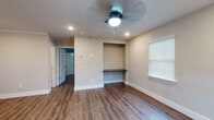 This single-floor home offers a clean, contemporary design with warm hardwood-style flooring running throughout every room, creating a cohesive and inviting atmosphere. The kitchen is a standout feature, showcasing white shaker-style cabinetry with crown molding, a neutral tile backsplash, stainless steel appliances including a refrigerator, electric range, microwave, and dishwasher, as well as a sink positioned beneath a window for natural light. The bedrooms are well-sized and finished with neutral-toned walls, ceiling fans with integrated lighting, and blinds-covered windows that allow for adjustable natural light. One bedroom features a built-in wall niche with a wooden desktop shelf, ideal for use as a dedicated workspace. An additional room includes a built-in dresser, adding practical storage to the layout. The bathroom is neatly appointed with a tub-shower combination surrounded by classic white subway tile, warm-toned fixtures, and wood-look flooring that ties the space together with the rest of the home. Throughout the space, bright white trim and baseboards provide a crisp contrast to the warm wall tones, contributing to the home's polished and move-in-ready presentation.