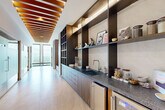 Located at 1081 Juniper St NE in Atlanta's Midtown neighborhood, this single-floor wellness suite is a masterfully designed retreat that blends luxury materials with purposeful function. The space is defined by a long, gallery-style corridor featuring striking wood-slat ceiling details with integrated lighting, large-format light stone tile flooring, and floor-to-ceiling windows that frame expansive city views at the far end.

Along one wall, custom dark-toned built-in shelving and cabinetry with granite countertops, an undermount sink, and a beverage refrigerator create a refined service and display area. Frosted glass doors with warm wood framing provide privacy access to the individual treatment and utility rooms. A built-in bench with a granite seat and warm wood cabinetry below offers a welcoming arrival moment, accented by decorative wall sconces.

The spa-style bathroom features a freestanding soaking tub set against floor-to-ceiling wood-look porcelain tile paneling, complemented by a gold towel stand and an adjacent stone bench for a serene, minimalist aesthetic. A dedicated sauna room is lined in light cedar with tiered bench seating, under-bench ambient lighting, and a signature Himalayan salt tile accent wall that bathes the room in a soft, warm glow. Together, these spaces compose a cohesive and tranquil wellness environment.