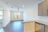 This well-designed single-floor unit offers a clean, contemporary aesthetic throughout, combining functional layout with modern finishes. The open-concept living and kitchen area forms the heart of the space, where warm wood-toned flooring flows seamlessly underfoot and recessed lighting keeps the interior bright and welcoming. A ceiling fan anchors the living area, which is bathed in natural light from a large window offering views of lush, tree-lined surroundings.

The kitchen is thoughtfully appointed with light wood cabinetry extending to the ceiling for ample storage, granite countertops, a subway tile backsplash, and a full suite of stainless steel appliances including a gas range, over-the-range microwave, refrigerator, and dishwasher. A peninsula with a granite overhang provides additional workspace and a natural division between the kitchen and living area.

The bedroom is a calm, airy retreat featuring hardwood-style flooring, a ceiling fan, and a generously sized window that invites natural light and treetop views. The bathroom is finished in crisp white tile, featuring a soaking tub and shower combination equipped with polished chrome grab bars for added accessibility and safety. The entryway is clean and direct, with easy access to all areas of the unit, creating a practical and comfortable flow throughout the home.