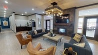This single-floor amenity facility is thoughtfully designed to blend comfort, style, and functionality across several distinct areas. The central lounge serves as the heart of the space, featuring a dramatic reclaimed wood accent wall with a built-in fireplace and mounted television. A statement chandelier with Edison bulbs hangs overhead, illuminating an arrangement of charcoal sofas, cognac leather chairs, and a patterned area rug. Adjacent to the lounge is a dedicated coffee bar, outfitted with dark cabinetry, subway tile backsplash, open wood shelving, and a commercial-grade Starbucks coffee machine. A casual gathering area nearby features high-top tables and bar-height seating, separated from an adjoining kitchen by sliding reclaimed wood barn doors. A media lounge with deep teal walls, curated wall art, and leather seating offers a more intimate retreat. The fitness center is well-equipped with treadmills, ellipticals, and a dedicated studio space for cycling and functional training. A standout feature is the HDi multi-sport simulator room, complete with a full projection screen and putting turf. Additional seating areas with brick accent walls and dark cabinetry with beverage coolers round out the offerings, creating a cohesive and upscale environment throughout.