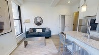 This 1-bedroom, 1-bathroom residence is thoughtfully laid out across a single floor, combining comfort and modern design. The open-concept living and dining area serves as the heart of the home, featuring light hardwood-style flooring, crisp white walls, and exposed beam detailing along the ceiling that adds a subtle architectural character to the space. Natural light fills the room, enhancing the clean and airy ambiance. The living area provides ample space for relaxing and entertaining, flowing seamlessly into the kitchen zone, which is equipped with a granite or stone-topped breakfast bar with seating — ideal for casual dining. The kitchen area connects effortlessly to the rest of the living space, reinforcing the open and inviting layout. A closet conveniently positioned off the main living area offers practical storage solutions. The bedroom and bathroom complete the unit, providing private and functional retreats. Throughout the residence, the design palette remains neutral and contemporary, with modern fixtures and finishes that create a cohesive, polished look. This unit is well-suited for those seeking a comfortable, efficiently designed living space with stylish touches.