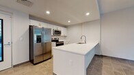 Located at 2409 Old Bradenton Rd in Sarasota, Florida, this single-floor residence offers a clean, modern aesthetic with an open-concept design that promotes a comfortable and functional living experience. Durable large-format tile flooring runs throughout the unit, providing a cohesive and easy-to-maintain surface across all areas.

The kitchen is a standout feature, showcasing crisp white shaker cabinetry, bright white countertops, and a full suite of stainless steel appliances, including a side-by-side refrigerator with ice and water dispenser, an electric range, built-in microwave, and dishwasher. A generous kitchen island with an integrated sink adds both workspace and casual dining potential, while recessed lighting keeps the area well-illuminated.

The open layout connects the kitchen seamlessly to the living and dining areas, which benefit from natural light streaming through large windows and a sliding glass door that leads to an outdoor view of lush greenery. The living spaces are spacious and versatile, with neutral walls ready for personalization.

The bathroom is well-appointed with a white vanity, white countertop, framed mirror, and a glass-enclosed walk-in shower with tile surround and brushed nickel fixtures. Additional spaces include a bedroom with a walk-in closet, completing this well-designed, move-in-ready residence.