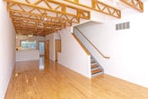 Located on Coolidge Highway in Royal Oak, Michigan, this three-floor residence offers a distinctive architectural character defined by soaring ceilings with exposed wood roof trusses, warm natural hardwood flooring throughout, and an abundance of natural light streaming through large vertical-blind windows with leafy outdoor views.

The kitchen is thoughtfully designed with light maple cabinetry, a peninsula with an integrated sink, stainless steel appliances including a gas range with overhead microwave, a white tile backsplash, and track lighting accented by the dramatic overhead truss work — creating a space that is both functional and visually striking.

Living and bedroom areas are generously proportioned, featuring polished hardwood floors, clean white walls, and windows that invite natural light. The upper level benefits from the full height of the exposed truss ceiling, adding an airy, loft-like quality to the space.

The bathrooms are finished with light maple vanities, tile flooring, and chrome fixtures. One bathroom includes a tub/shower combination, while another features a dedicated walk-in shower stall with built-in shelving. An in-unit laundry area with a full-size washer and dryer provides added convenience. Throughout, the consistent use of natural wood tones and neutral finishes creates a cohesive, modern aesthetic.