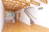 Located on Coolidge Highway in Royal Oak, Michigan, this three-floor residence offers a distinctive architectural character defined by soaring ceilings with exposed wood roof trusses, warm natural hardwood flooring throughout, and an abundance of natural light streaming through large vertical-blind windows with leafy outdoor views.

The kitchen is thoughtfully designed with light maple cabinetry, a peninsula with an integrated sink, stainless steel appliances including a gas range with overhead microwave, a white tile backsplash, and track lighting accented by the dramatic overhead truss work — creating a space that is both functional and visually striking.

Living and bedroom areas are generously proportioned, featuring polished hardwood floors, clean white walls, and windows that invite natural light. The upper level benefits from the full height of the exposed truss ceiling, adding an airy, loft-like quality to the space.

The bathrooms are finished with light maple vanities, tile flooring, and chrome fixtures. One bathroom includes a tub/shower combination, while another features a dedicated walk-in shower stall with built-in shelving. An in-unit laundry area with a full-size washer and dryer provides added convenience. Throughout, the consistent use of natural wood tones and neutral finishes creates a cohesive, modern aesthetic.