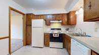 Located on Fairfax Court NW in Canton, Ohio, this single-floor home offers a practical and comfortable layout with consistent finishes throughout. The kitchen is well-equipped, showcasing rich oak cabinetry with classic hardware, a tile backsplash, light countertops, and white appliances including a refrigerator, electric range, and dishwasher. Tile flooring runs through the kitchen, providing durability and ease of maintenance. The home features multiple carpeted rooms with neutral walls and warm wood trim accents along the baseboards and door frames, lending a cohesive, understated aesthetic. Bedrooms are generously sized, with natural light provided by windows dressed in wood trim, and include built-in closets with bifold doors for ample storage. The bathrooms are cleanly finished with tile flooring, oak vanities topped with light countertops, a medicine cabinet mirror, and a full tub-and-shower combination in the main bath. A hallway connects the living areas to the private rooms, and a thermostat and wall vent are conveniently positioned near the entry. Baseboard heating is present throughout the carpeted rooms. The overall layout is straightforward and well-maintained, offering a move-in-ready environment with classic, functional design elements throughout.