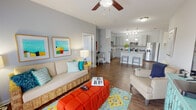 This single-story residence in Youngsville, Louisiana, offers a well-designed open-concept layout that seamlessly connects the living, dining, and kitchen areas. The living room is a spacious, light-filled space featuring wood-style flooring, a ceiling fan, and French doors that invite natural light while providing access to the outdoors. The kitchen is a standout feature, equipped with gray shaker-style cabinetry, granite countertops, stainless steel appliances, and a central island with bar seating. Pendant lighting and a track light fixture illuminate the workspace effectively. A hallway entry leads directly into the open kitchen and living area, providing a welcoming transition into the home. Both bedrooms are carpeted and include ceiling fans, with the primary bedroom offering a walk-in closet and an en-suite bathroom. The bathrooms feature granite countertops, undermount sinks, and wood-style flooring. Each bedroom also benefits from natural light through well-positioned windows. The walk-in closets provide generous storage with full-width rod systems. The overall design presents a clean, contemporary aesthetic with soft gray walls and consistent finishes throughout.