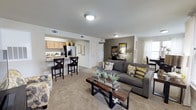 Located at 6216 66th St in Lubbock, Texas, this single-floor residence offers a thoughtfully designed open-concept layout that seamlessly connects the main living and kitchen areas. The living room is carpeted and features a neutral color scheme accented by a warm taupe feature wall, providing a cozy yet contemporary ambiance. A gray sectional sofa, complemented by yellow and patterned accent pillows, anchors the space, while a rustic wood-and-metal coffee table adds an industrial touch. Natural light filters in through window treatments, brightening the interior. The kitchen is positioned adjacent to the living area and is equipped with light wood cabinetry, a stainless steel refrigerator with built-in ice and water dispenser, and dark countertops. A breakfast bar with two bar-height chairs provides a casual dining option and serves as a natural dividing element between the kitchen and living spaces. The layout promotes an open flow throughout, making the home feel spacious and well-connected. Overhead flush-mount lighting fixtures illuminate both spaces efficiently. The overall design balances functionality with a welcoming aesthetic, making this single-level home a practical and comfortable living environment.