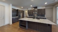 This well-appointed 2-bedroom, 2.5-bathroom single-floor residence offers a generous and thoughtfully designed living space with modern finishes throughout. The open-concept kitchen serves as the centerpiece, featuring dark espresso cabinetry, granite countertops, a large center island with an undermount sink, stainless steel appliances, and a striking geometric tile backsplash. Rich hardwood flooring flows through the main living and kitchen areas, creating a warm and cohesive aesthetic. The spacious living room is bright and airy, with natural light filtering in through windows with outdoor views and a ceiling fan overhead. The primary bedroom suite offers plush carpeting, a ceiling fan, and ample natural light, and is complemented by a walk-in closet with dual shelving sections and a luxurious en-suite bathroom. The primary bath features a double-sink vanity with dark cabinetry and quartz countertops, a large framed mirror, tile flooring, and a glass-enclosed walk-in shower. The secondary bathroom is equally well-finished, with a tall dark wood storage tower, an undermount sink vanity, and clean modern fixtures. A dedicated laundry room includes a washer and dryer, granite folding counter, and additional shelving for storage, rounding out this highly functional and refined living space.