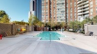 Located at 255 Huguenot St in New Rochelle, NY, this pool and bathroom space offers a combination of functional design and modern amenities. The outdoor pool area features a generously sized rectangular pool with clear blue water, surrounded by a wide, light-toned concrete deck that provides ample space for lounging. The area is enclosed by fencing and accented by mature trees, offering a degree of privacy while maintaining open views of the neighboring high-rise buildings under open skies.

The bathroom is finished in a clean, contemporary style with white tile flooring and neutral-toned walls that create a bright, airy atmosphere. A white vanity with an undermount sink, chrome fixtures, and a large mirror with integrated lighting serves as the focal point, offering both practicality and a polished look. The tub-shower combination is lined with crisp white subway tiles and fitted with a striped shower curtain that adds a subtle design accent. Chrome towel bars are mounted along the walls, and the overall layout is efficient and well-organized. The space is finished with attention to detail, conveying a clean and welcoming ambiance throughout.