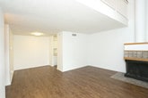 This two-story residence at 7414 Elgin Ave in Lubbock, Texas offers a well-organized layout across two distinct levels. The main floor features a spacious living area with rich wood-look flooring, a textured ceiling, and a corner fireplace accented with tile surround and wood trim — serving as a natural focal point of the room. A large window allows natural light to fill the space, creating a bright and welcoming atmosphere. The galley-style kitchen is efficiently designed with ample white cabinetry trimmed in warm wood tones, generous counter space, wood-look flooring, and full appliance provisions including a refrigerator, dishwasher, and range. A full bathroom on the lower level includes a vanity with stone-look countertop, tub/shower combination with white tile surround, and wood-look flooring. The staircase, featuring a warm wood handrail and white baluster railing, leads to the upper level, where carpeted open areas offer flexible living or sleeping space. The upper floor also includes an open loft-style area with soft carpeting and a ceiling fan, overlooking the lower level through the open railing. Throughout, the interior maintains a clean, neutral palette with white walls and consistent finishes that lend a cohesive, move-in-ready feel.
