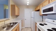 Located at 130 Cumberland Way in Pataskala, Ohio, this single-floor residence offers a practical and well-organized living space. The kitchen is designed in a classic galley layout, maximizing efficiency with cabinetry lining both sides of the room. Light oak wood cabinets provide ample storage above and below the countertops, lending a warm and inviting tone to the space. The kitchen is equipped with white appliances, including a refrigerator, electric range, built-in microwave, and dishwasher, all positioned for convenient workflow. Light-toned countertops complement the cabinetry, while a stainless steel sink adds a practical touch. The light tile flooring is easy to maintain and ties the space together cohesively. Overhead lighting illuminates the kitchen evenly, ensuring a bright and functional environment. A six-panel interior door at the end of the kitchen leads to an adjoining area, contributing to the home's straightforward and efficient floor plan. The textured ceiling adds a subtle visual detail consistent throughout the space. Overall, the residence presents a clean, functional, and comfortable living environment well-suited to everyday life in the Pataskala community.