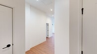 This single-floor unit offers a well-organized layout with a clean, contemporary design characterized by crisp white walls, warm hardwood-style flooring, and recessed lighting throughout. The space is thoughtfully arranged, with open hallways connecting the various rooms and allowing for a smooth, cohesive flow.

The kitchen is a functional centerpiece, featuring white flat-panel cabinetry extending to the ceiling for ample storage, dark countertops, a classic white subway tile backsplash, and a full suite of stainless steel appliances including a range, microwave, dishwasher, and refrigerator. A matte black faucet at the double-basin sink adds a modern accent.

The hallways are notably tall and airy, with high ceilings that enhance the sense of openness. Individual rooms offer natural light through large black-framed windows with urban views, further brightening the neutral interiors.

Two bathrooms are present: one features a taupe vanity with white countertop, framed mirror, and a soaking tub with white tile surround and matte black fixtures; the other includes a glass-enclosed walk-in shower with matching matte black hardware. Light tile flooring completes both bathrooms. The overall ambiance is modern, clean, and move-in ready.