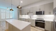 Located at 525 J Place in Plano, Texas, this thoughtfully designed one-bedroom, one-bathroom residence offers a clean, contemporary aesthetic across a single, well-organized floor. Light wood flooring flows throughout the main living areas, complemented by crisp white walls and modern finishes that create a bright, inviting atmosphere.

The kitchen is a standout feature, showcasing sage-toned shaker-style cabinetry with sleek matte black hardware, white quartz countertops, a full suite of stainless steel appliances including a gas range, built-in microwave, dishwasher, and French door refrigerator, and a classic subway tile backsplash. A central island provides additional prep and dining space, while pendant lighting adds a stylish focal point overhead.

The bedroom is carpeted for comfort and benefits from tall windows dressed with white blinds that allow generous natural light to fill the room. It connects directly to a walk-in closet outfitted with built-in shelving and hanging rods for efficient storage.

The bathroom is elegantly appointed with a dual-sink vanity featuring gray cabinetry and matte black fixtures, a wide backlit mirror, light wood flooring, and marble-look tile surrounding the tub and shower surround. The overall design is cohesive, modern, and move-in ready.