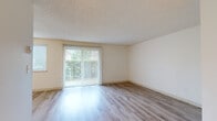 Located at 16677 NE Russell St in Gresham, Oregon, this 2-bedroom, 1-bathroom unit offers a practical and comfortable single-floor layout. The living room is a standout space, featuring light wood-style laminate flooring that runs throughout the main areas, neutral cream-toned walls, a textured ceiling, and a large sliding glass door dressed with vertical blinds that floods the room with natural light and provides views of the surrounding greenery.

The kitchen is efficiently arranged in a U-shaped configuration, outfitted with warm oak-toned cabinetry — both upper and lower — a white electric range, a full-size refrigerator, a built-in sink, and an overhead exhaust hood. Light wood flooring continues into the kitchen, maintaining a cohesive feel throughout the main living areas.

Both bedrooms are carpeted in a neutral beige tone, offering a softer, quieter feel. The primary bedroom is a comfortable size and includes sliding wood-panel closet doors providing ample storage. A secondary bedroom features light wood flooring and a window fitted with horizontal blinds for natural light control. The hallway connects the rooms efficiently, and a full bathroom serves the unit. Overall, this home presents a clean, functional layout suited for everyday living.