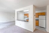 This single-floor residence offers a practical and comfortable layout designed for everyday living. The expansive living area is finished with neutral wall-to-wall carpeting and benefits from an abundance of natural light streaming through a large sliding glass door that opens to an outdoor area, framing pleasant views of surrounding trees and greenery.

The kitchen is thoughtfully connected to the living space via a pass-through window with a dark speckled countertop ledge, creating an open and communicative feel between the two areas. Inside, the kitchen is equipped with warm oak cabinetry extending from floor to ceiling, dark laminate countertops, a stainless steel sink, a white gas range, and a full-size refrigerator, providing ample storage and functional workspace.

The bedrooms are generously sized and carpeted, each featuring wide windows that invite natural light and offer leafy outdoor views, contributing to a calm and restful atmosphere. The bathroom is clean and well-appointed, featuring an oak vanity with a white countertop and integrated sink, a mirrored medicine cabinet, and a full tub-shower combination with white tile surround. Throughout the residence, the light-toned walls and soft carpeting create a cohesive, understated aesthetic that is both inviting and easy to personalize.