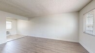 This single-floor, 2-bedroom, 1-bathroom residence offers a practical and well-organized layout with a clean, neutral aesthetic throughout. The living room is an open, airy space featuring light wood-look laminate flooring, crisp white walls, and a textured ceiling, providing a versatile canvas for any furnishing style. Natural light filters in through a window fitted with horizontal blinds, creating a welcoming atmosphere. A wall-mounted heating unit adds a functional element to the room.

The kitchen is efficiently designed, featuring white shaker-style cabinetry extending to the ceiling for ample storage, dark granite-style countertops, a stainless steel refrigerator, and a gas range. Light ceramic tile flooring and a window with blinds keep the space bright, while a wall-unit air conditioner provides climate control.

Both bedrooms are outfitted with wood-look flooring and ceiling fans with light fixtures. The primary bedroom includes a mirrored sliding-door closet that enhances the sense of space, along with a window that brings in natural light. The second bedroom is comparably sized and similarly finished.

The bathroom is clean and straightforward, featuring tile flooring, a full bathtub-shower combo, and a toilet in a bright white finish. A connecting hallway ties the rooms together in a cohesive and functional floor plan.