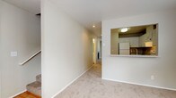 This two-floor residence offers a well-organized layout with a neutral color palette and carpet flooring throughout the main living and bedroom areas. The living room serves as a central gathering space, anchored by a tile-surround fireplace with a white mantel and sliding glass door access to an outdoor balcony, allowing natural light to filter in.

The kitchen is efficiently designed with white cabinetry, granite-style countertops, a full suite of white appliances including a refrigerator and electric range, and a pass-through window that connects to the main living area. Wood-look flooring runs through the kitchen and bathroom spaces.

The bedrooms are carpeted and well-sized, with multiple rooms featuring sliding closet doors that provide ample storage. One bedroom includes a walk-in style closet, while baseboard heaters are present throughout for individual climate control. Windows with blinds bring in natural light across the upper level.

The bathroom includes a full tub and shower with white tile surround, a vanity with granite-style countertops, white cabinetry, and wood-look flooring. A dedicated laundry room houses a full-size washer and dryer with overhead shelving, adding everyday convenience to the home.