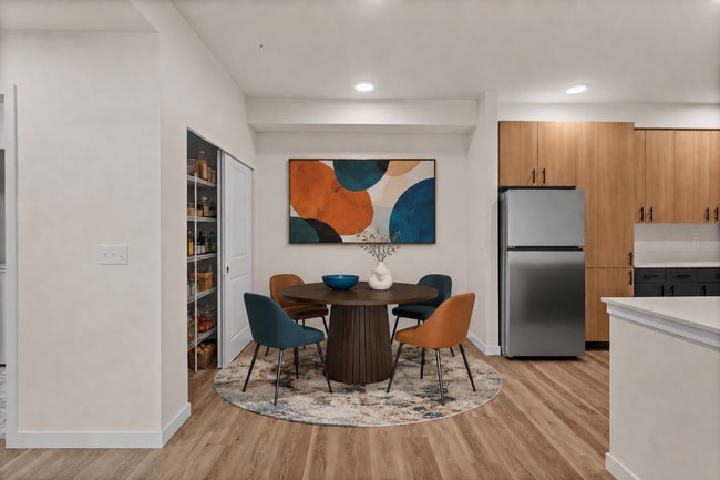 Staged dining room with a round table, four chairs, an area rug, abstract artwork, and a stocked open pantry. - 27 West Apartments