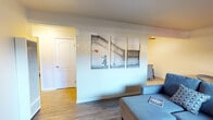 This single-floor unit offers a functional and thoughtfully arranged layout that balances comfort with everyday practicality. The living area serves as the heart of the space, featuring wood-style flooring and a striking triptych wall art display — a reproduction of Banksy's iconic "Girl with Balloon" — that adds a contemporary artistic flair. Sliding glass doors flood the room with natural light and open directly to a private enclosed patio, ideal for outdoor relaxation. A glass-top dining table with a sculptural chair rounds out the living and dining area. The galley-style kitchen is efficiently designed with white cabinetry, granite-look countertops, a stainless steel sink, and white appliances, including a range and refrigerator, all set atop light tile flooring. The bathroom features a full tub and shower combination with floor-to-ceiling large-format beige marble-style tile, lending a clean and polished look. The primary bedroom is a serene retreat with warm wood-style flooring, neutral tones, and symmetrical bedside lamps creating a calm ambiance. The second bedroom offers a window with natural light and a wall-mounted air conditioning unit for personalized climate control. Throughout, the unit maintains a cohesive, neutral palette with clean lines and practical finishes.