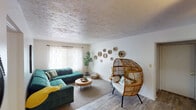 This single-floor residence offers a thoughtfully designed layout with a warm, eclectic aesthetic throughout. The living room serves as the heart of the home, featuring textured ceilings, light wood-style flooring, and sheer curtained windows that invite soft natural light. Woven wall accents and a distinctive rattan egg chair contribute to the space's relaxed bohemian character, complemented by a plush tufted sectional sofa. An adjacent dining area provides additional versatility, complete with a ceiling fan and a creative bicycle-frame bar table set atop a vibrant floral area rug. The kitchen is well-appointed with rich dark wood cabinetry, marble-look countertops, and a full suite of stainless steel appliances including a gas range, built-in microwave, and dishwasher — all set on light wood-style flooring. The primary bedroom is bathed in natural light from multiple windows dressed in sheer white curtains, with plush carpeting and a warm wood dresser adding a classic touch. A second bedroom offers a cozy, carpeted retreat with closet access and its own cheerful personality. Together, these rooms create a cohesive, livable space with distinct character in every corner.