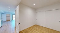 Located at 1112 Locust Ave in Long Beach, California, this thoughtfully designed unit offers a clean, modern aesthetic across a single floor. Light wood flooring runs throughout the main living areas, complementing the bright white walls and recessed lighting that give the space an open, airy feel.

The combined kitchen and living area forms the heart of the unit. The kitchen is outfitted with sleek white cabinetry, white quartz countertops, and stainless steel appliances including a gas range, over-the-range microwave, and a stacked washer and dryer unit. A textured tile backsplash adds visual depth against the otherwise minimalist palette. The living area is generously proportioned, offering a versatile open canvas for various furniture arrangements.

The bathroom features terrazzo tile flooring, a modern vanity with white countertop and integrated sink, matte black hardware and mirror frame, and a separate shower area — all contributing to a refined, contemporary look.

The sleeping area includes access to a dedicated walk-in closet with built-in shelving, providing practical storage. A large sliding glass door opens to a private balcony, flooding the room with natural light and offering pleasant views of the surrounding Long Beach neighborhood, with palm trees and rooftops visible in the distance.