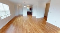 This single-floor space offers a seamless open-concept layout that effortlessly connects the living area, entryway, and kitchen into one cohesive, welcoming environment. Warm-toned hardwood flooring extends throughout, lending a sense of continuity and natural elegance to the entire floor plan.

The spacious main living area is bathed in natural light and features crisp white walls accented by classic crown molding, creating a polished, refined aesthetic. A stylish chandelier serves as a focal point overhead, adding a touch of sophistication to the open layout.

The kitchen is clearly defined within the open floor plan and showcases rich, dark wood cabinetry paired with stainless steel appliances, including a built-in microwave and dishwasher. A window above the sink allows natural light to fill the cooking space, while the overall design balances functionality with visual warmth.

The entryway, visible from the main living space, offers a clean and welcoming introduction to the home, complete with a solid white door and a flush-mount light fixture. The transition between spaces feels natural and unobstructed, highlighting the thoughtful flow of the layout. Overall, the space combines classic design details with modern convenience to create a comfortable and inviting environment.