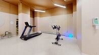 Located at 1412 Seymour Street in Halifax, Nova Scotia, this wellness studio offers a thoughtfully designed, open-concept fitness space that balances functionality with an inviting atmosphere. The studio occupies a single floor, providing a generous, unobstructed workout area finished with durable terrazzo-style flooring that is both practical and easy to maintain.

The space is anchored by a full-wall mirror installation, which enhances the sense of openness and supports dance, barre, and movement-based workouts. A freestanding ballet barre adds to the studio's versatility, making it suitable for a range of fitness disciplines. Cardio equipment, including a treadmill and stationary spin bike, lines one section of the floor, while a tiered dumbbell rack provides a well-organized free weights station. A wall-mounted flat-screen display adds a multimedia element to the environment.

The industrial-style exposed ceiling features painted ductwork and overhead fluorescent strip lighting, creating bright, even illumination throughout. A wall-mounted split air conditioning unit ensures comfortable year-round climate control. An elevated staircase entry with a metal railing adds a distinctive architectural element, leading down into the main floor. A motivational phrase — "Live well, Be well, Do well" — is inscribed on one wall, reinforcing the studio's wellness-focused identity. Ambient accent lighting adds a subtle, welcoming glow to the space.