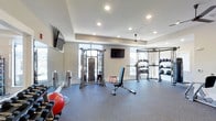 The weight room is a thoughtfully designed fitness space that provides a comprehensive environment for strength training and exercise. The room features a tray ceiling with recessed lighting, contributing to a bright and open atmosphere, while a ceiling fan ensures comfortable air circulation during workouts. Large windows along the walls allow ample natural light to fill the space, creating an energizing environment.

The flooring consists of durable gray rubber matting, ideal for heavy equipment and high-impact exercise. A wall-mounted mirror along one side expands the sense of space and allows users to monitor their form. Two flat-screen televisions are mounted on the walls, offering entertainment during workouts.

The room is equipped with a dual cable resistance machine, a multi-tiered dumbbell rack with a full range of free weights, a medicine ball rack stocked with various weighted balls, and an adjustable workout bench. Additional accessories include a stability ball and other training tools. The overall layout is spacious and well-organized, allowing multiple users to exercise simultaneously without feeling crowded.